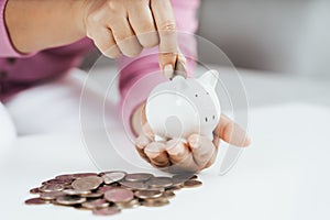 Close up of woman hand putting money coin into piggy bank for saving money. saving money and financial concept