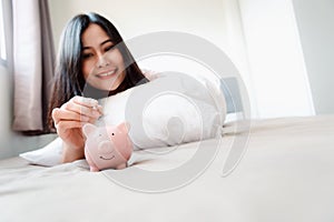 Close-Up Woman Hand is Putting a Money Coin into Piggy Savings on The Bedroom., Female Hand is Inserting Coin in Piggy Bank.