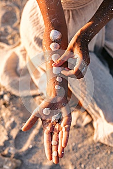 Close up of woman hand putting sea shells on other hand on the beach at sunset