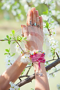 Close up woman hand with rings and bracelets in yoga mudra namaste gesture in front cherry blossom