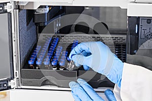 Close up woman hand in a rubber gloves put sample in a glass vial with blue cap into the autosampler rack in HPLC system
