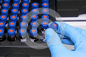 Close up woman hand in a rubber gloves put sample in a glass vial with blue cap into the autosampler rack in HPLC system