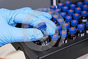 Close up woman hand in a rubber gloves put sample in a glass vial with blue cap into the autosampler rack in HPLC system