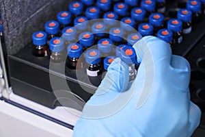 Close up woman hand in a rubber gloves put sample in a glass vial with blue cap into the autosampler rack in HPLC system