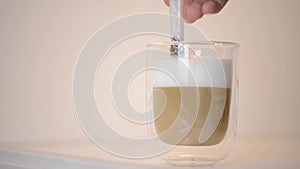 Close-up of woman hand stirring a fresh latte macchiato coffee with spoon in clear glass cup.