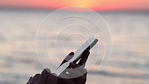 Close-up of a woman hand texting in a messenger or texting on a smartphone at an airport window. Silhouette of hands a