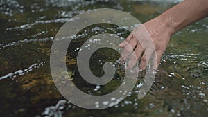 Close up woman hand touching the surface of the water in the forest river or lake