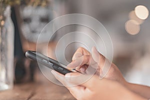 Close up woman hand using smart phone in cafe shop with bokeh light background