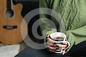 Close up of woman hand wearing winter sweater holding coffee cup while enjoying a moment of solitude at home