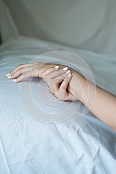 close up of woman hands and arms crossed on bed sheet with delicate soft natural light. Concept of hand care and manicure. natural