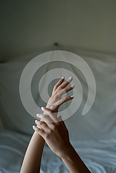 close up of woman hands and arms crossed on bed sheet with delicate soft natural light. Concept of hand care and manicure. natural