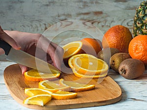 Close up woman hands cutting fresh orange with knife and wooden chopping board