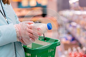 Close up of woman hands in gloves holding a shopping basket and choosing milk in a supermarket. Shopping during