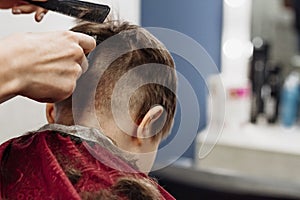 Close-up of woman hands grooming kid boy hair in barber shop.