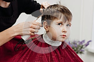 Close-up of woman hands grooming kid boy hair in barber shop.