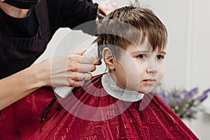 Close-up of woman hands grooming kid boy hair in barber shop.