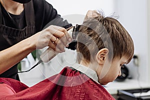 Close-up of woman hands grooming kid boy hair in barber shop.