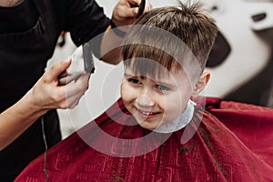 Close-up of woman hands grooming kid boy hair in barber shop