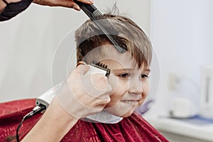 Close-up of woman hands grooming kid boy hair in barber shop.