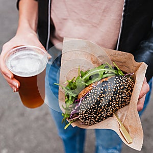 Close up of woman hands holding delicious organic salmon vegetarian burger and homebrewed IPA beer on open air beer an