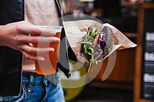 Close up of woman hands holding delicious organic salmon vegetarian burger and homebrewed IPA beer on open air beer an