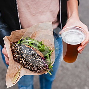 Close up of woman hands holding delicious organic salmon vegetarian burger and homebrewed IPA beer on open air beer an