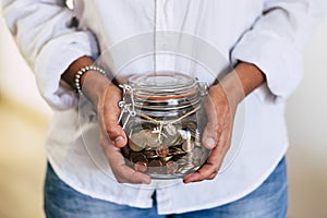 Close up of woman hands at home taking a transparent glass vase full of coins and airplane outside - economy and money for the