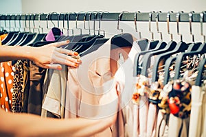 Close up woman hands make choice on colorful clothes on racks in a fashion boutique