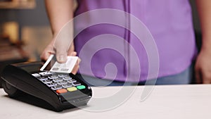 Close up of woman hands making payment with credit card machine terminal while swiping debit card to pay the bill. NFC