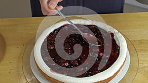 Close up of woman hands making sweet cherry cake with white cream and biscuit.