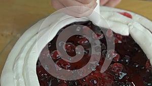 Close up of woman hands making sweet cherry cake with white cream and biscuit.