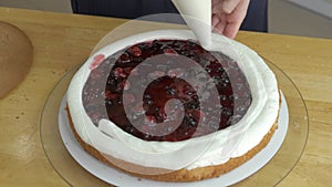 Close up of woman hands making sweet cherry cake with white cream and biscuit.