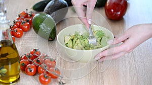 Close-up of woman hands mashing avocado with fork in bowl.