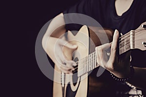 Close up of woman hands playing guitar in the dark background