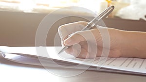 Close up of woman hands signing or writing a document on a sheet of white paper with black pen in the morning.