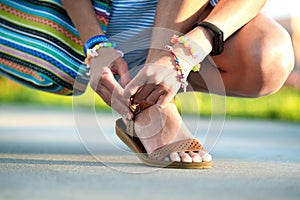 Close up of woman hands tying her open summer sandals shoes on sidewalk in sunny weather