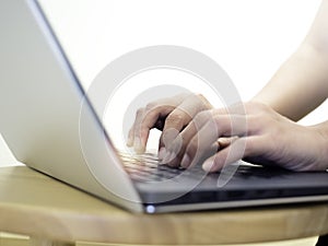 Close up of woman hands typing on laptop computer keyboard on round wood table.