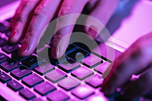 Close up woman hands typing on laptop keyboard, professional online gamer hand fingers on notebook keyboard in neon color, sitting