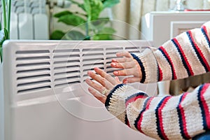 Close-up of woman hands warming near electric heating radiator