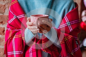Close-up woman hands wrapped warm plaid bright pink fuchsia, holding a mug enjoying free time, weekend at home, relaxing