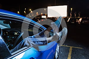 Close up of woman hanging her legs out of car window while watching a movie at drive in cinema from the front seat of