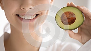 Close up woman with healthy toothy smile holding avocado