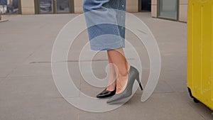 Close-up of a woman in high-heeled shoes with a suitcase walking along the road.