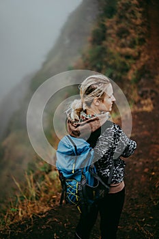 Close up of woman hiker with blue backpack on the narrow misty path of mountain ridge on Santo Antao island, Cape Verde