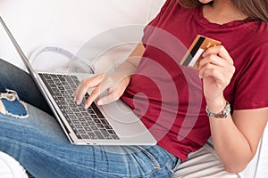 Close up woman holding credit card and use laptop shopping online on sofa in house.digital payment marketing technology concept