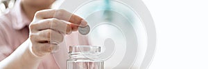 Close-up of a woman holding a drop of coins in a glass jar, she is accounting for income and expenses and dividing her savings.