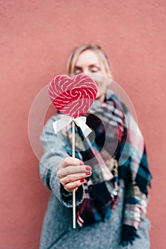 Close-up of a woman holding a heart shaped caramel lollipop.