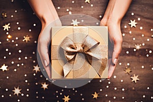 Close up of a woman holding a luxury gift box present wrapped with gold ribbon and golden glitter