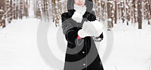 Close-up of woman holding natural soft white snow in her hands to make a snowball, smiling during a cold winter day in