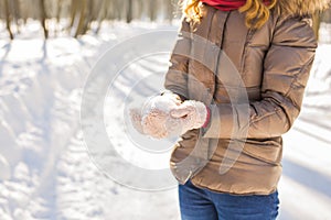 Close-up of woman holding natural soft white snow in her hands to make a snowball, smiling during a cold winter day in